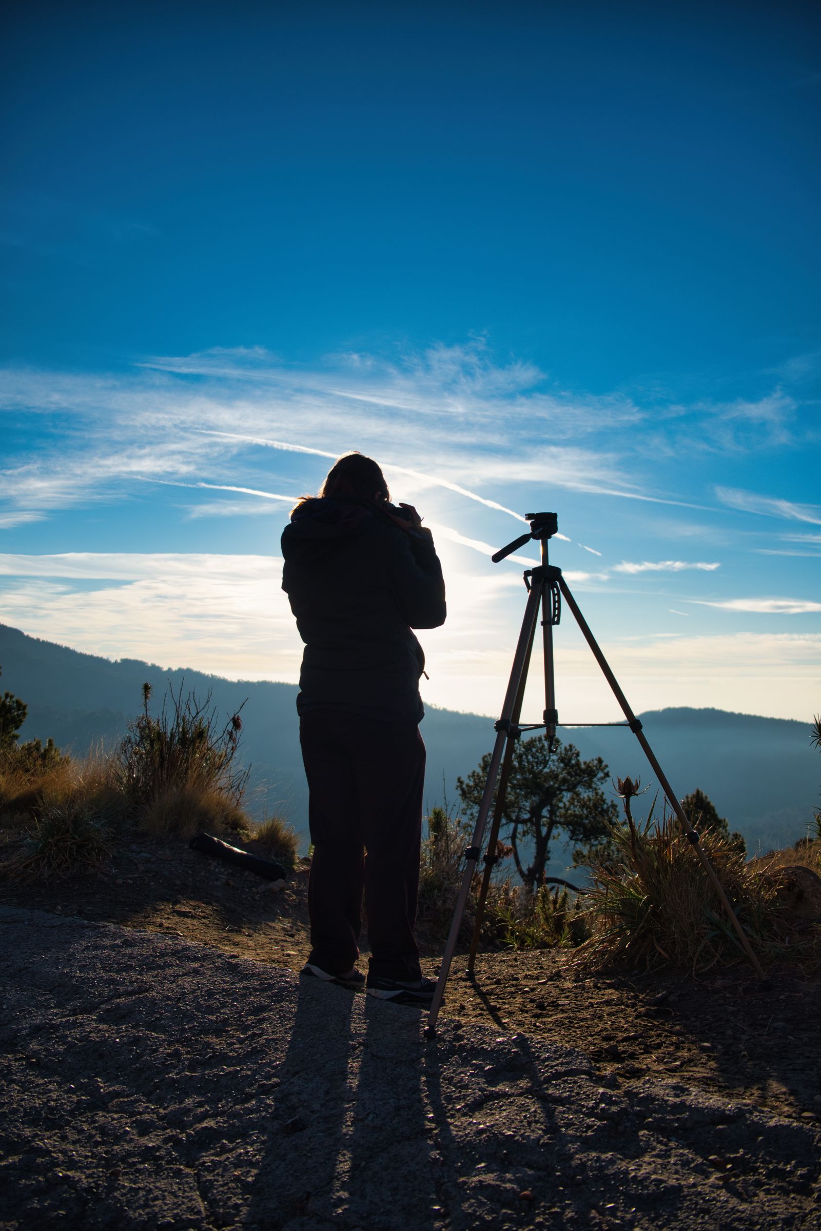 Fotograf mit Stativ bei Sonnenaufgang in einer Berglandschaft